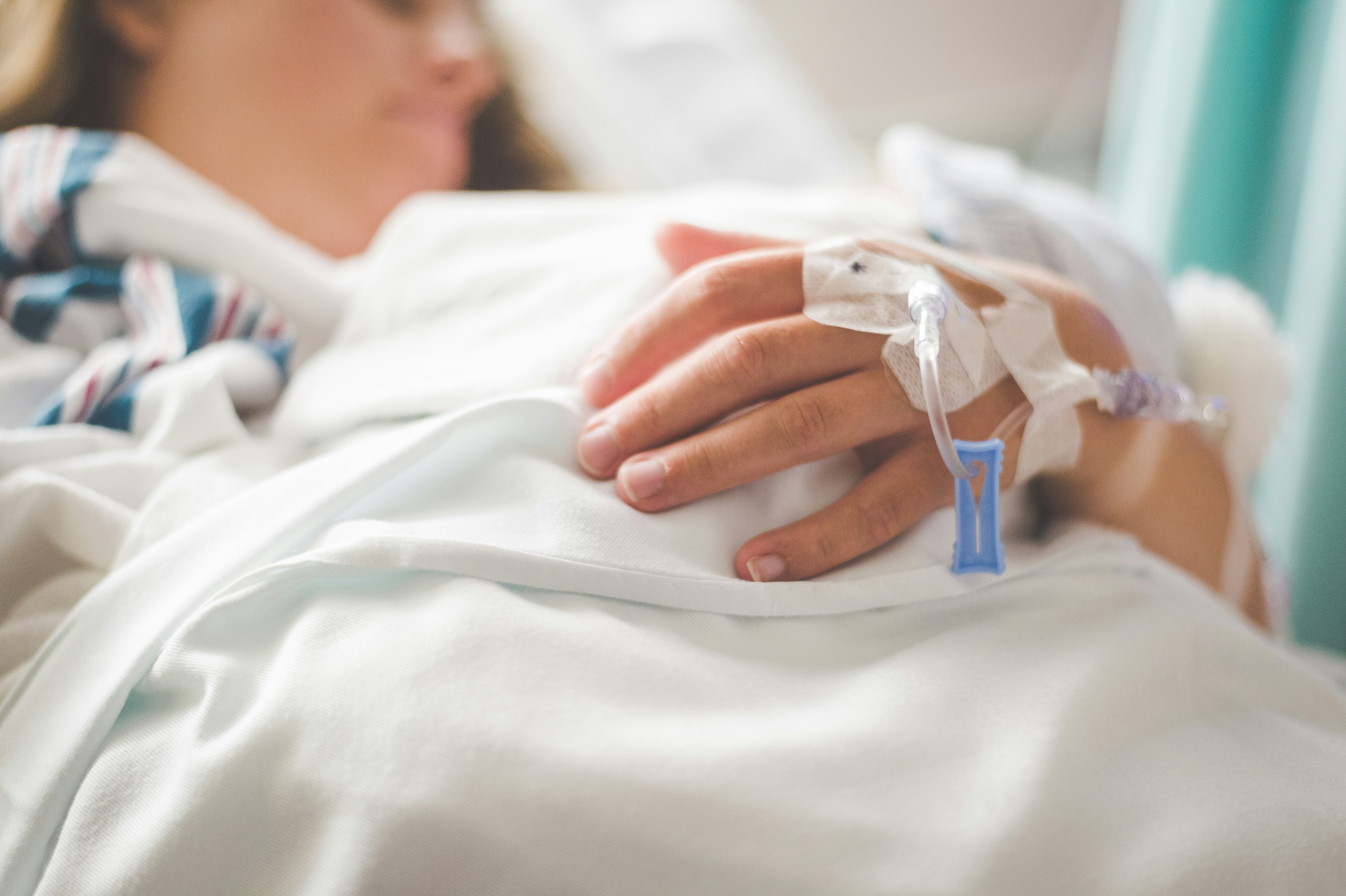 A photograph of a woman laying in a hospital bed with an iv in her hand